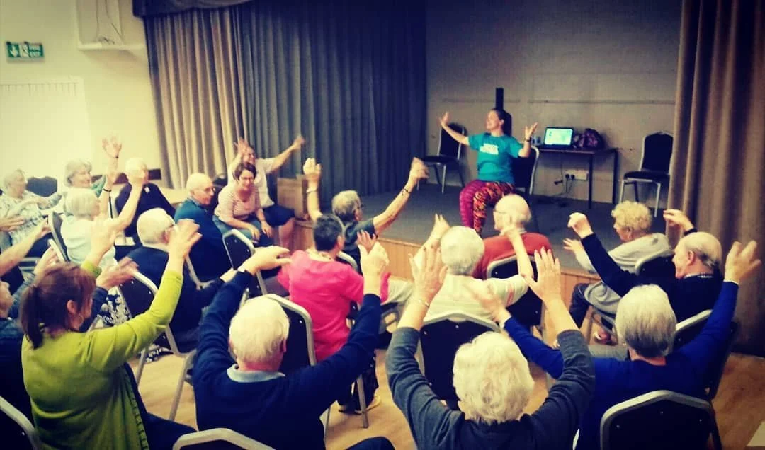 Care home residents smiling during a seated dance session