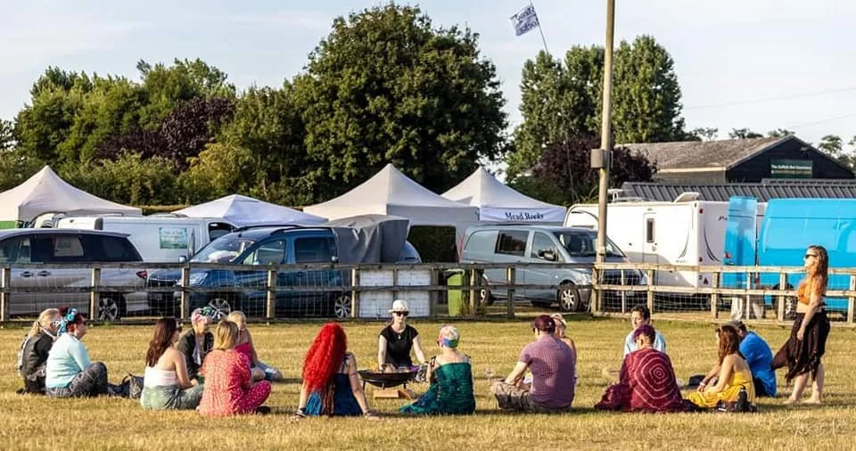 A festival circle gathered on the grass among camper vans and tents