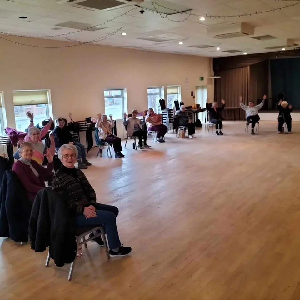 Smiling group in a seated dance class, arms out wide